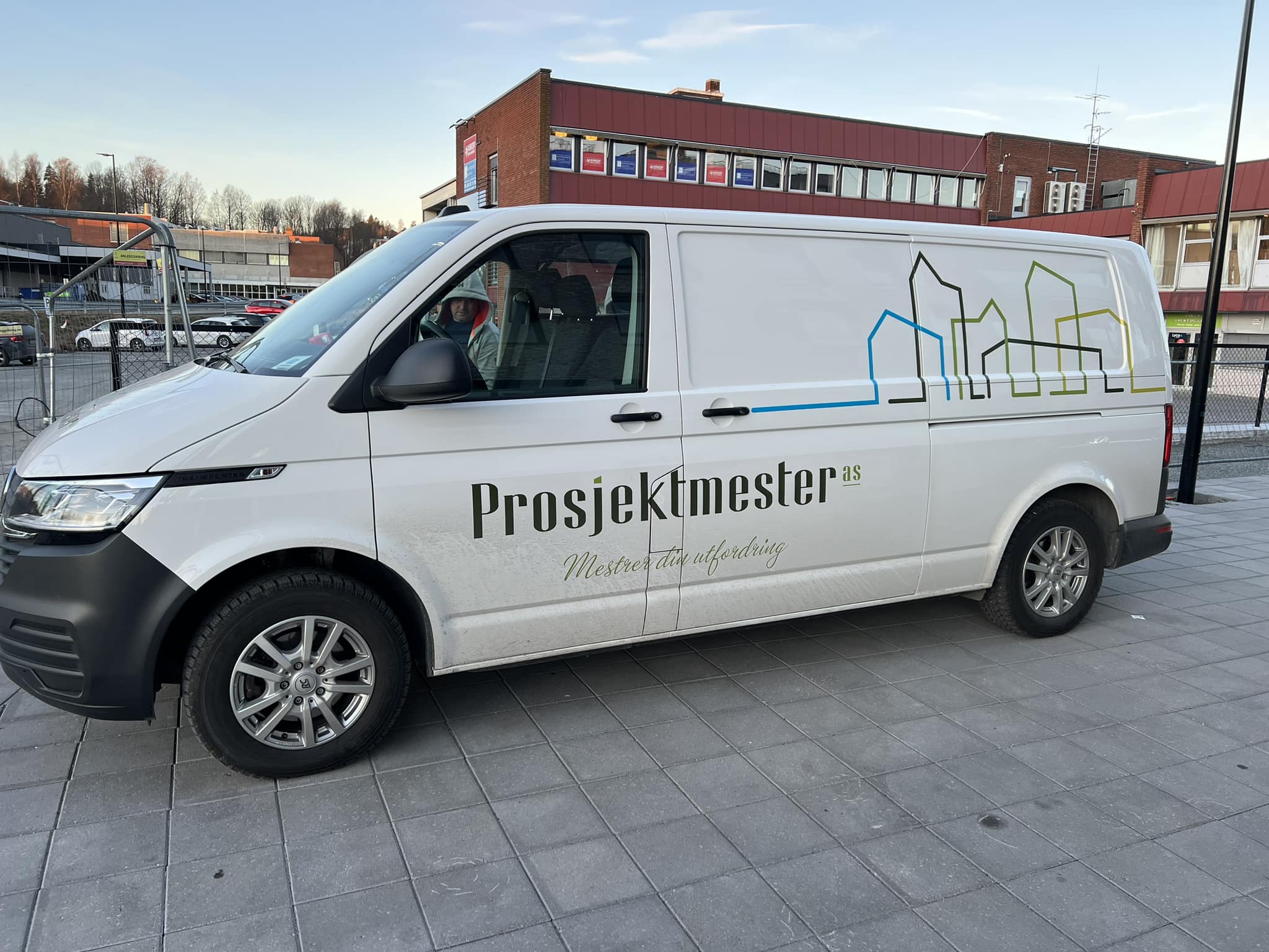 Hvit firmabil med prosjektmester as logo utenfor byggeplass